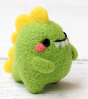 A green needle felted dino toy with yellow spikes, pink cheeks, and white pointy teeth