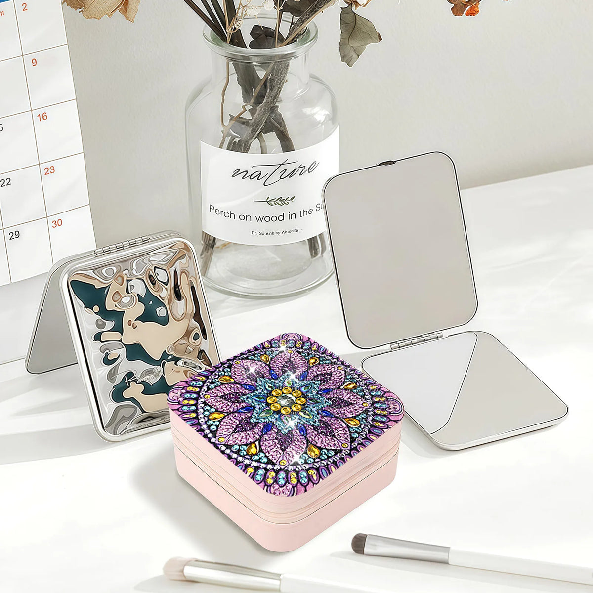 A pink square jewelry case with a colorful diamond art mandala pattern on the lid in purples, blue, and gold
