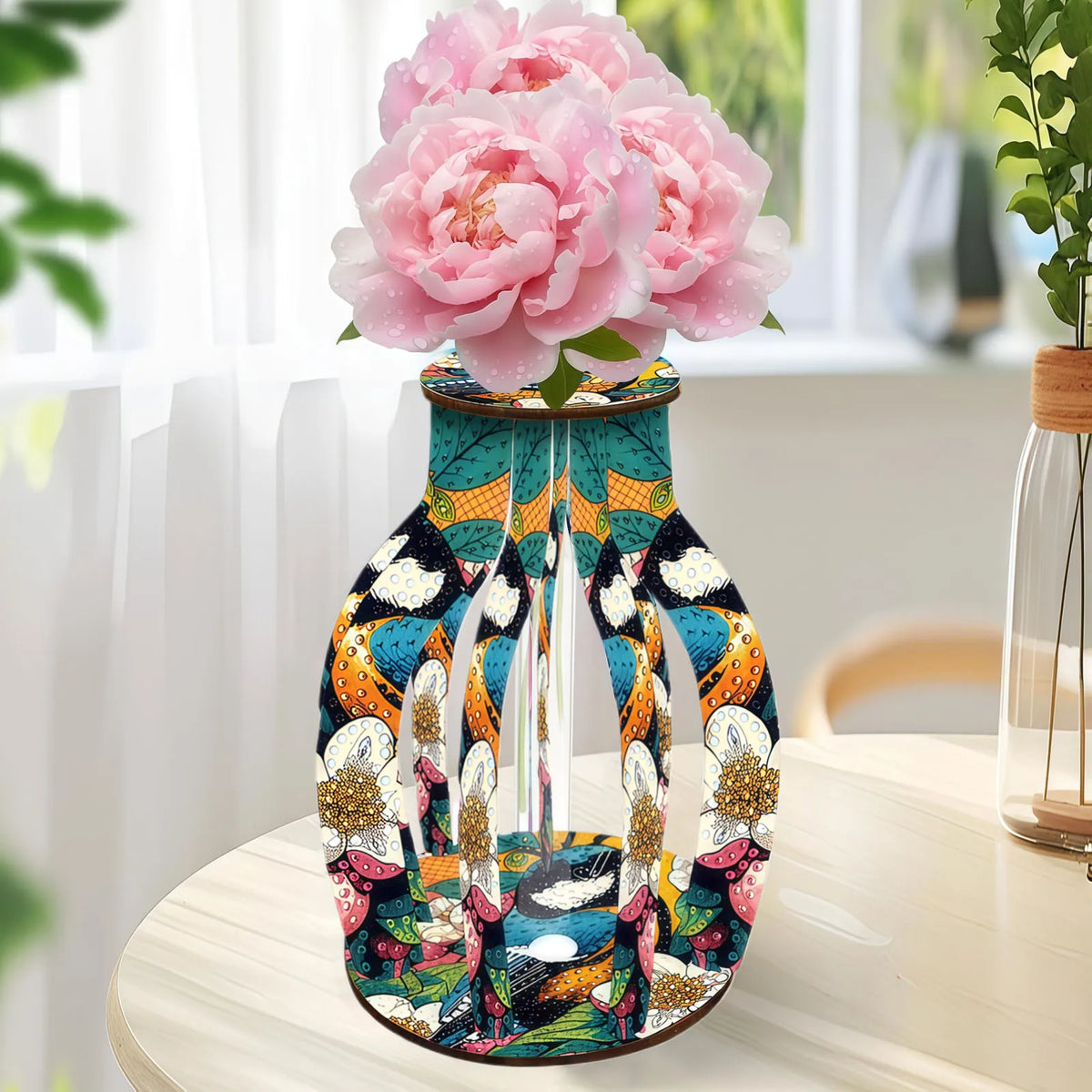 A decorative vase with a colorful abstract and floral pattern, holding pink peony flowers