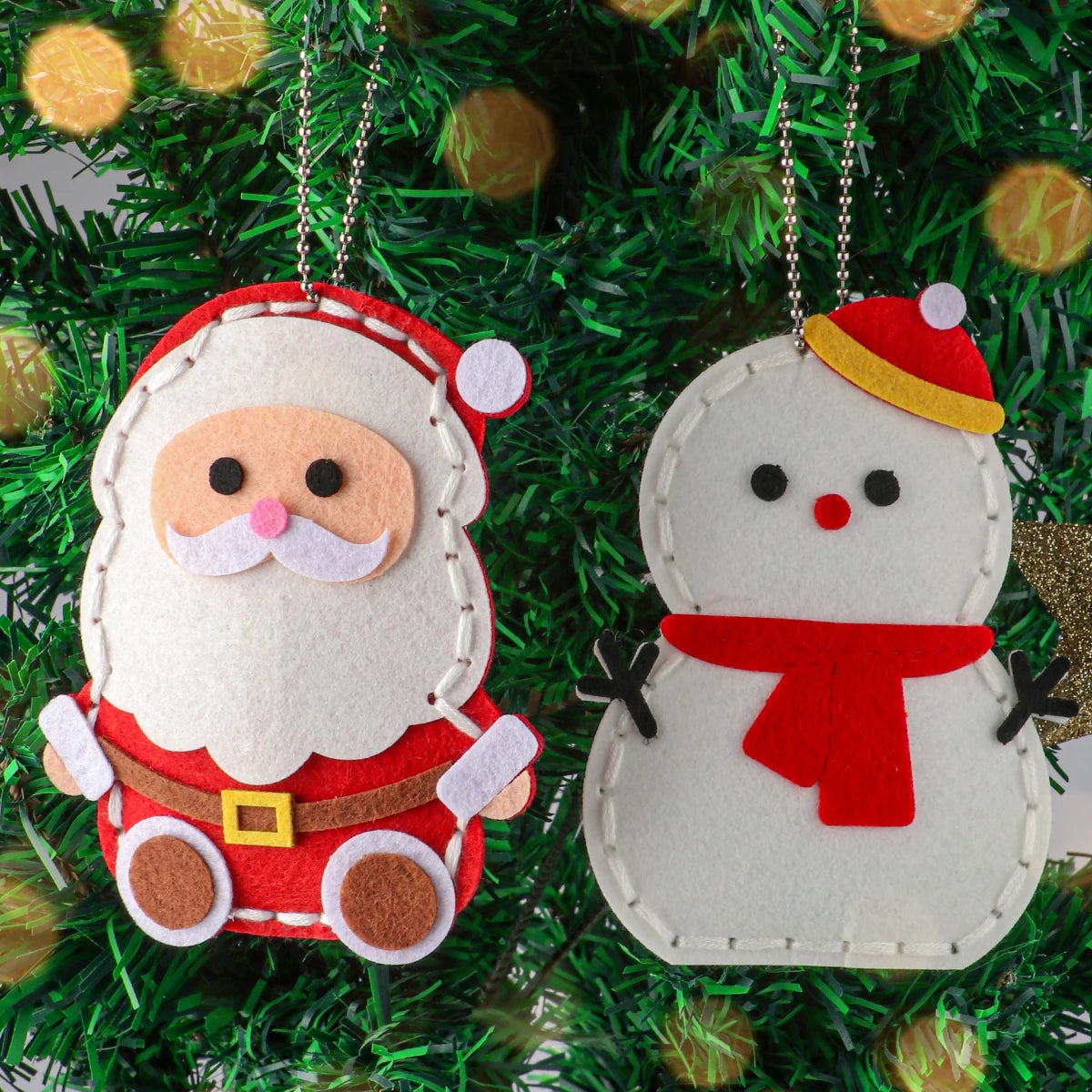 Two handmade felt Christmas tree ornaments hanging on a green Christmas tree. One ornament is Santa Claus in a red suit with a white beard, and the other is a snowman wearing a red scarf and hat.