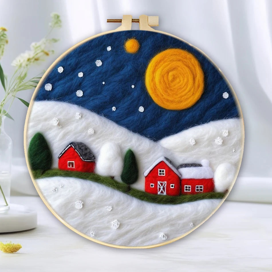 Needle felted winter night scene with a full moon, stars in the sky, with a red barn and red house in snowy white hills in a hoop frame.