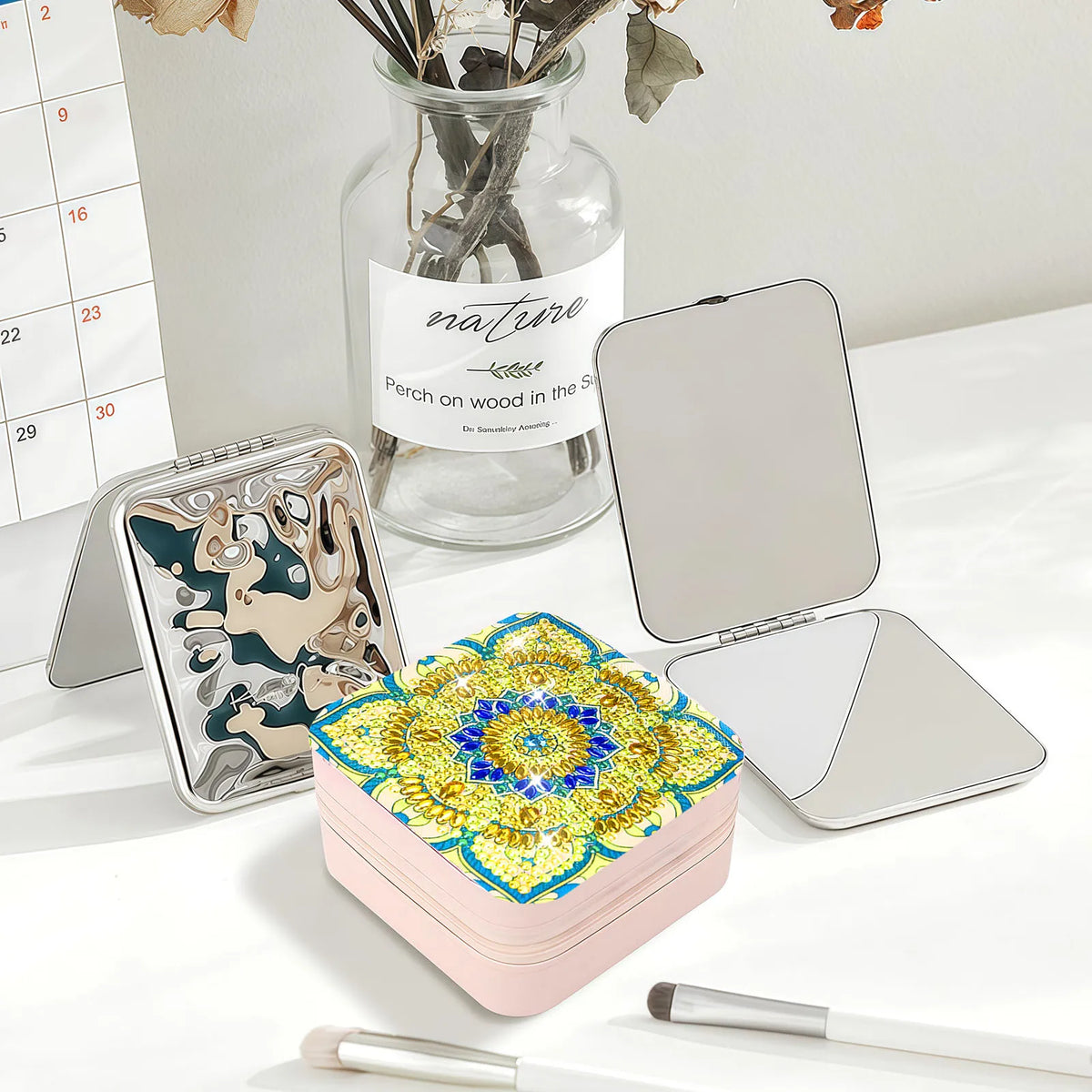 A pink square jewelry case with a colorful diamond art  mandala design on the lid in blues, yellow and gold