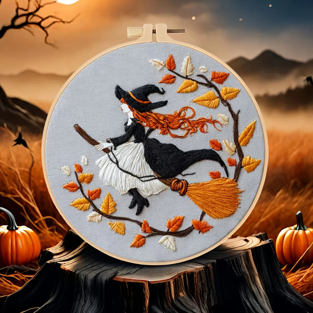 A circular embroidery hoop displays a an embroidered design of a witch riding a broomstick among autumn leaves. 