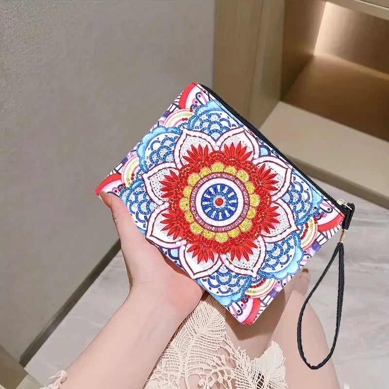 A hand holds a rectangle zip pouch with a colorful diamond art mandala pattern in red, blue, yellow, and white, featuring a black wrist strap