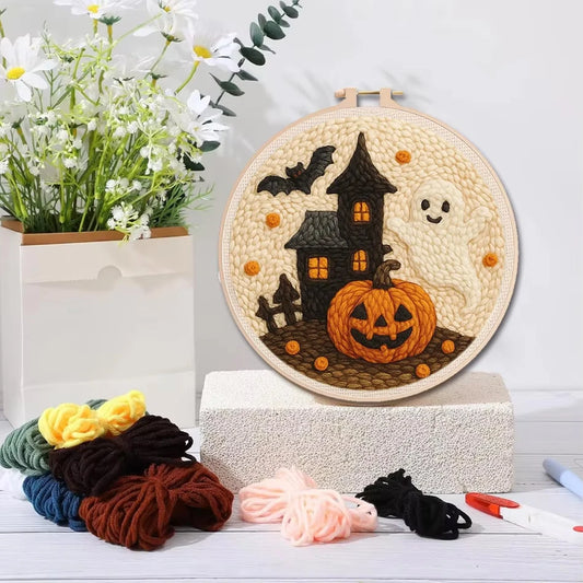 A circular embroidery hoop displaying a completed Halloween-themed punch needle design with a black haunted house, orange jack-o'-lantern, white ghost, and bats on a cream fabric background. 