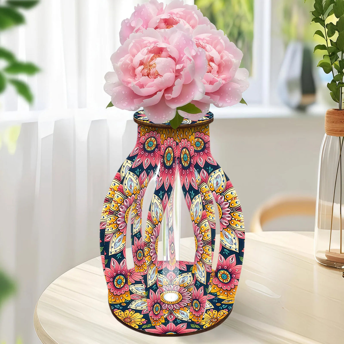 A decorative glass vase with a colorful floral and geometric pattern, filled with large pink peony flowers
