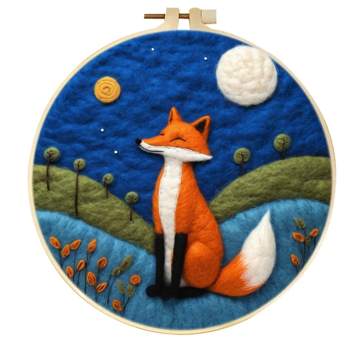 Needle felted red fox sitting under a full moon with a dark blue sky, green hills and some flowers in a hoop frame