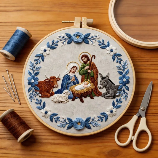 A circular embroidery hoop, featuring a nativity scene stitched with blue, white, green, brown, and gold thread. 