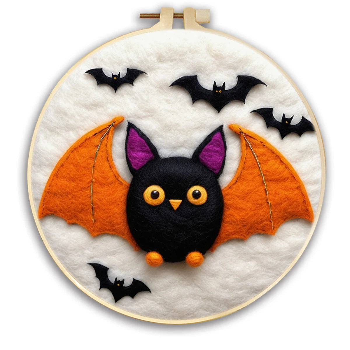 A circular embroidery hoop displays a cute bat-themed needlepoint or felt artwork. The design features a black bat face with yellow eyes and a small orange nose, purple inner ears, and large orange wings, set against a white background with three small black bats.