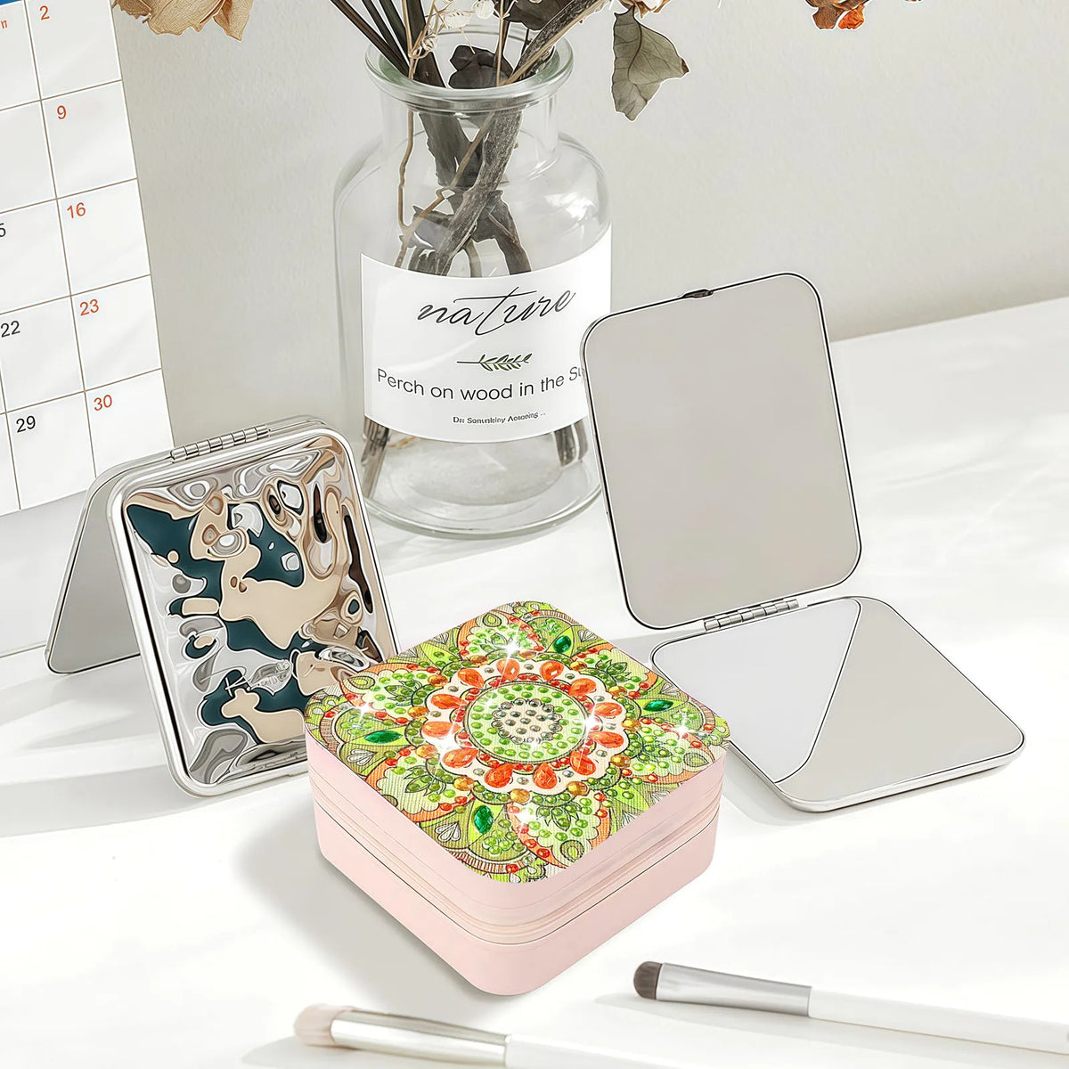 One closed jewelry case with a pink base and a colorful mandala pattern on top in reds, greens, and cream