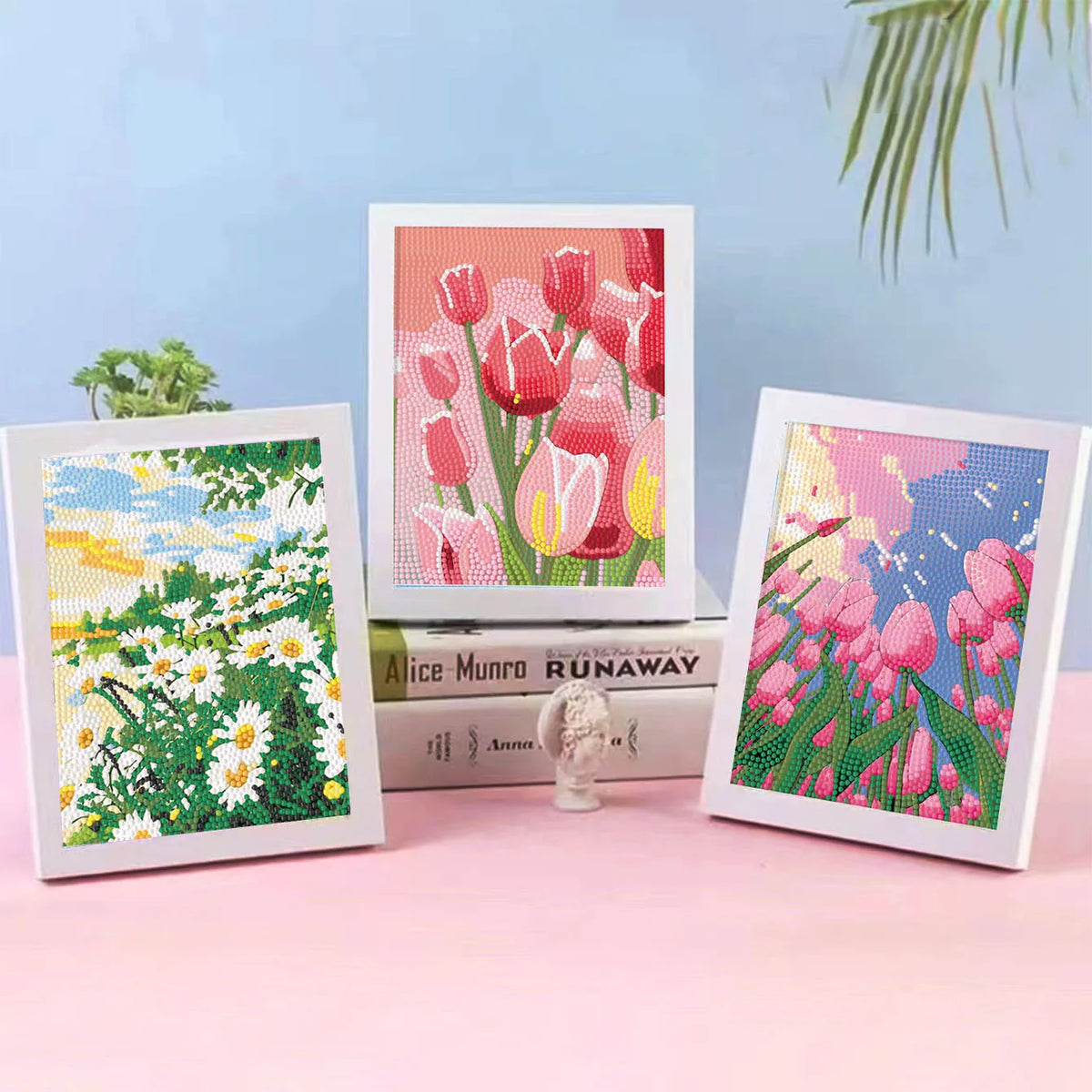 Three framed diamond painting art . The center print shows pink tulips, flanked by a white daisy landscape on the left and a pink flower field on the right.