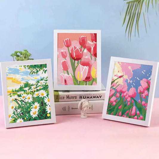 Three framed diamond painting art . The center print shows pink tulips, flanked by a white daisy landscape on the left and a pink flower field on the right.