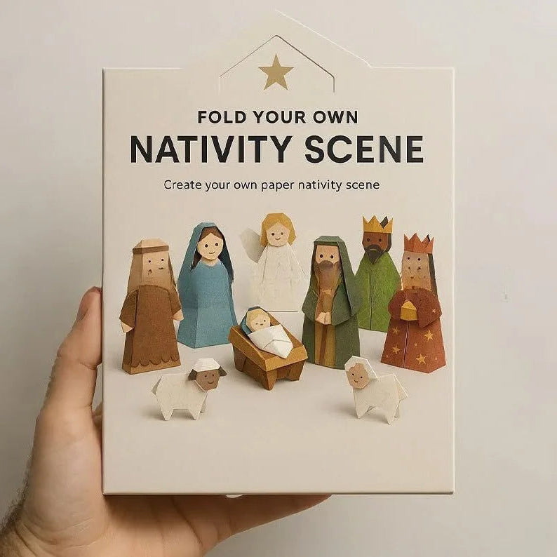 A hand holds a white box for a fold-your-own paper nativity scene. The front of the box shows colorful illustrated figures of the Holy Family, wise men, an angel, and shepherds, with the text 'NATIVITY SCENE' and 'FOLD YOUR OWN' visible.