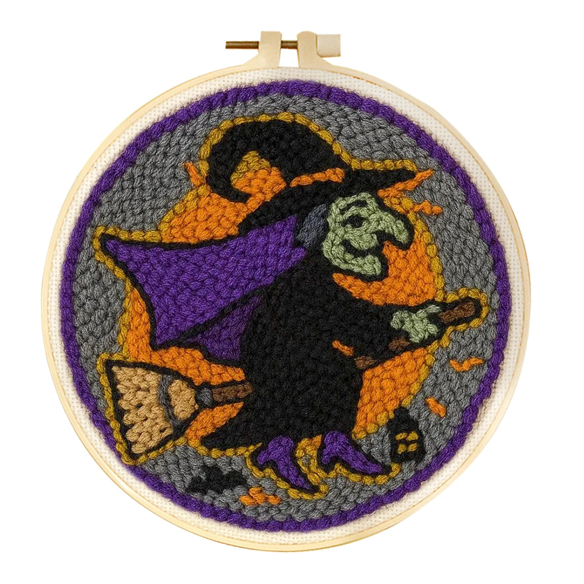 A circular needlepoint embroidery hoop featuring a witch riding a broomstick against a gray and orange circular background. The punch needle design includes purple, black, beige, and green details 