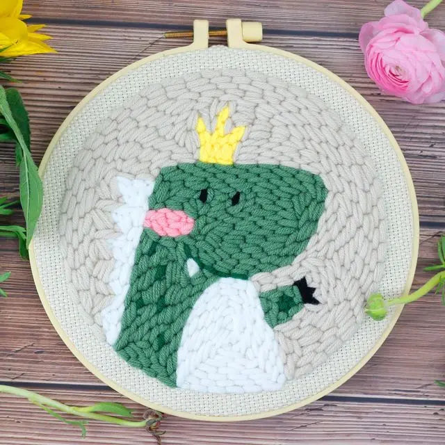 Embroidery hoop with a green dragon design on a wooden surface with flowers.