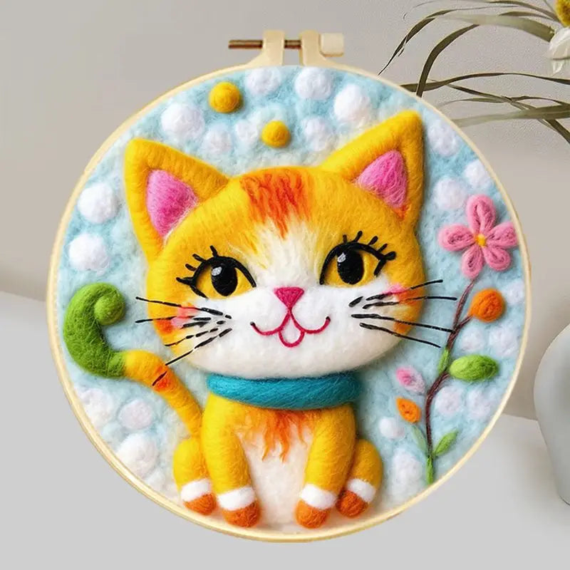 Needle felted smiling orange cat wearing a blue collar in a hoop frame with and blue and white background and some flowers