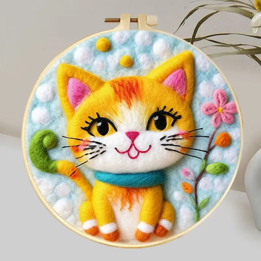 Needle felted smiling orange cat wearing a blue collar in a hoop frame with and blue and white background and some flowers