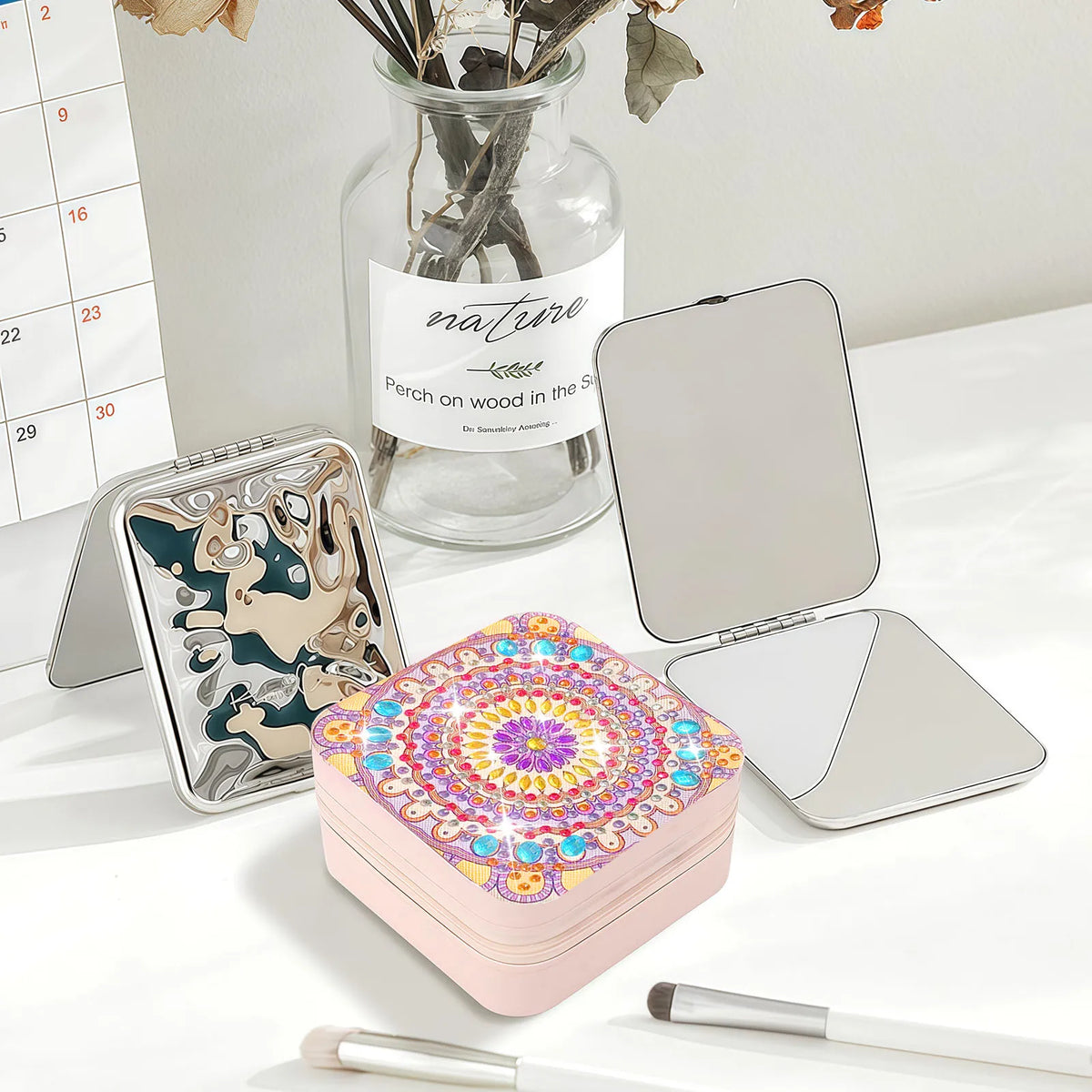 A pink square jewelry case with a colorful diamond art mandala pattern on the lid in purple, yellow, red and blue