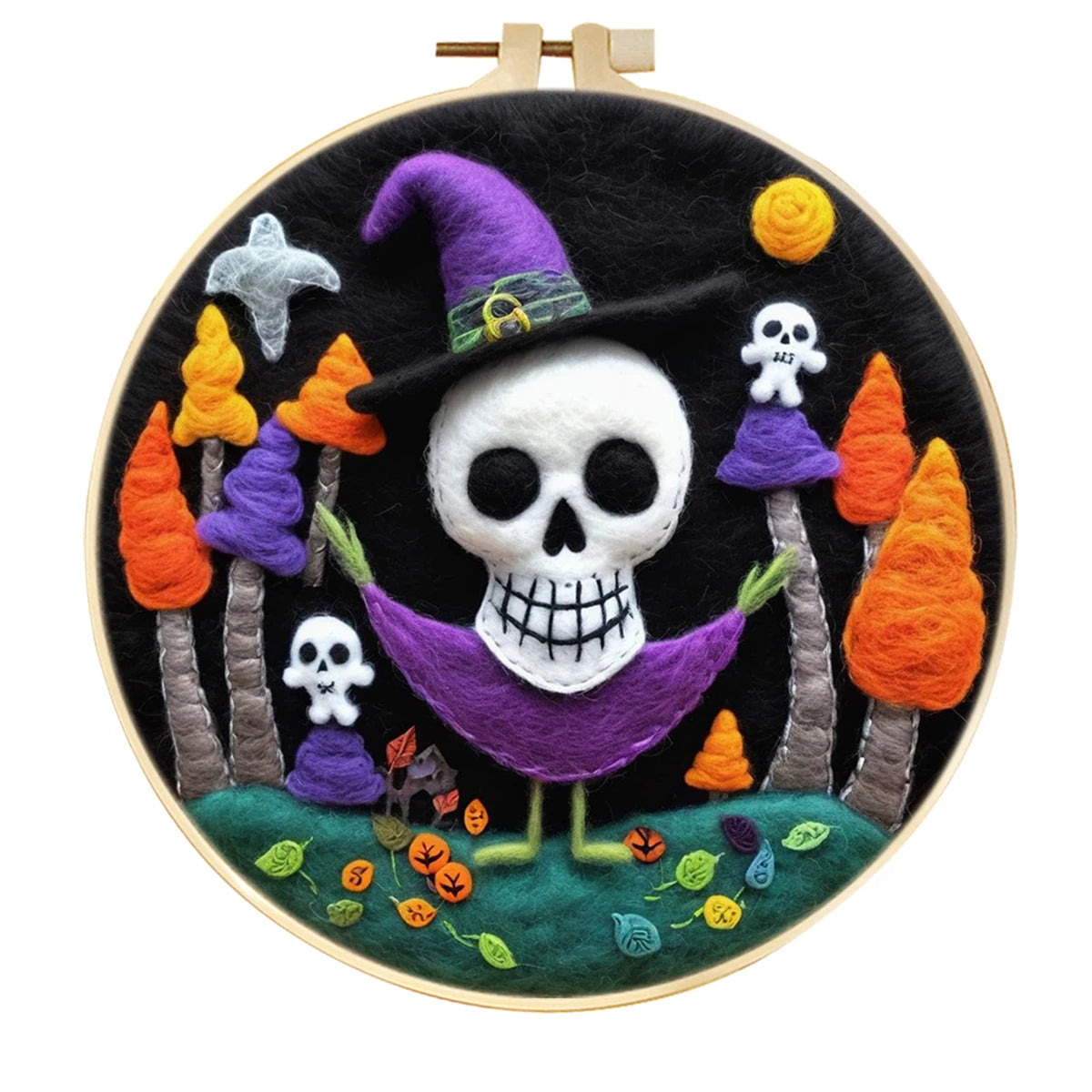 A circular needle felted Halloween themed artwork in a wooden hoop, featuring a white skull wearing a purple witch hat and purple hammock, surrounded by orange and purple trees, small white skulls, a gray bird, and a green ground with scattered autumn leaves