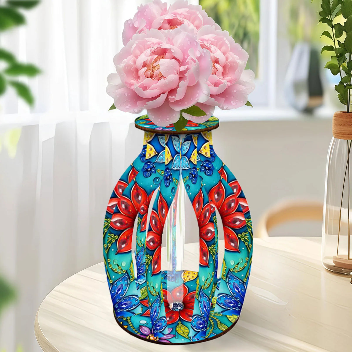 A colorful diamond art vase with a vibrant floral pattern in red, blue, yellow, and green, filled with pink peony flowers