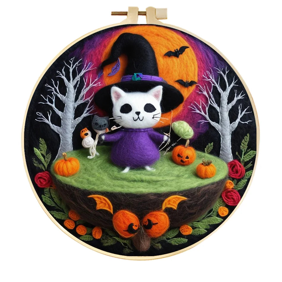 Embroidery hoop with a Halloween-themed needle felted design featuring a cat in a witch costume, pumpkins, and bats.