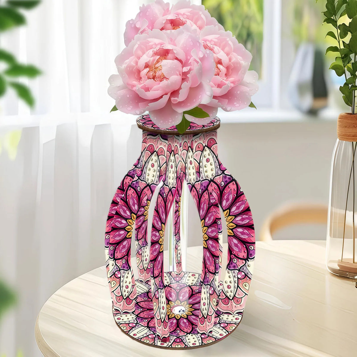 A decorative ceramic vase with a pink, purple, and white floral mandala pattern, filled with large pink peony flowers